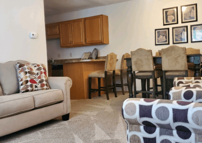 A cozy living room featuring a couch, chairs, and an open kitchen area, creating a welcoming atmosphere for gatherings.